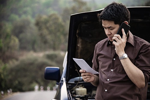 a man looking at a piece of paper and on the phone with a personal injury lawyer documenting the car accident