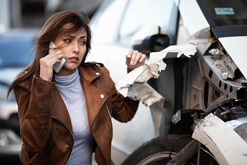 a distressed brunette woman in a car accident calling her personal injury lawyer and looking at the damages