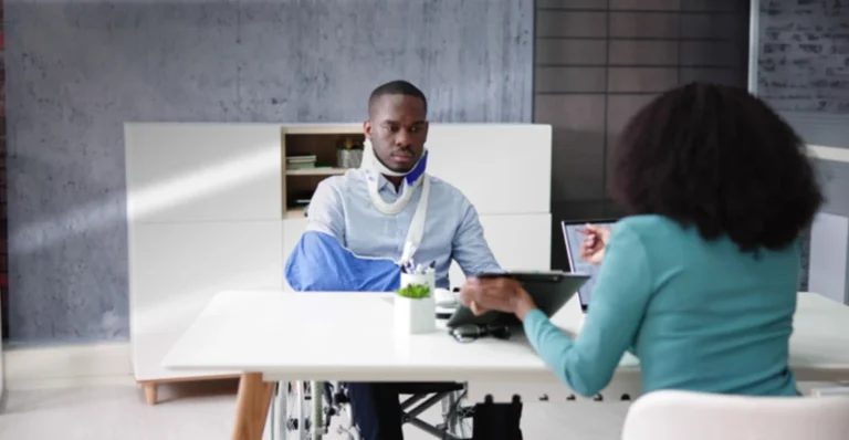 Injured client with neck brace and arm sling consulting with professional about personal injury case in modern office setting