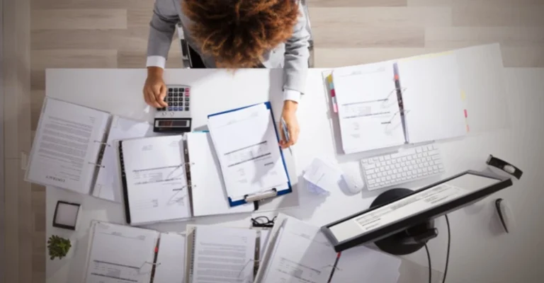 Professional calculating financial damages using multiple binders of documentation and calculator for personal injury case evaluation